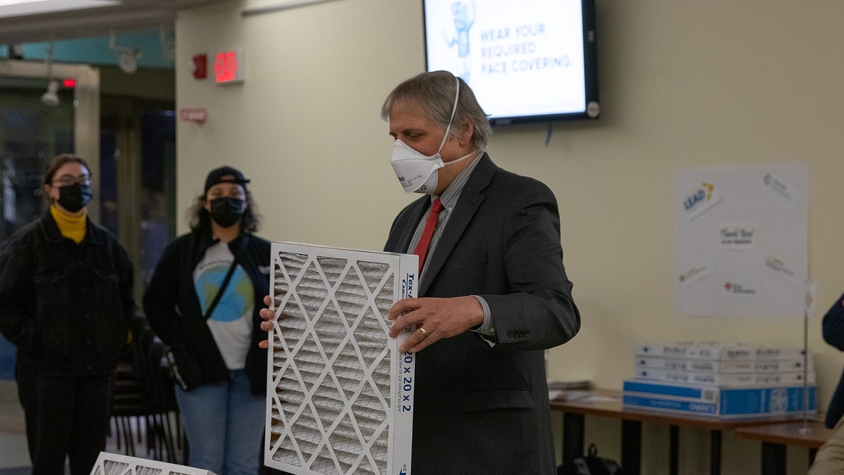 A man in an N95 mask holds a 20 by 20 inch pleated air filter at a Corsi-Rosenthal box building event at UC Davis